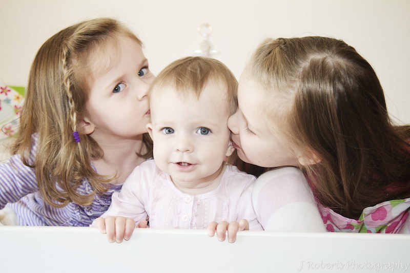 1 year old girl getting kisses from her older sisters - family portrait photography sydney